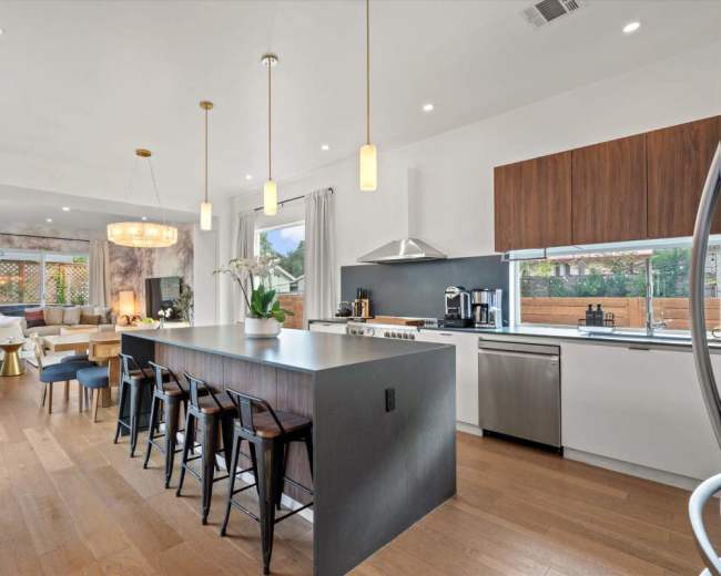 A modern kitchen features a large island with seating, sleek appliances, and a dining area that opens to a living space with natural light.