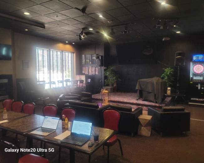 The image shows a venue setup for a performance, featuring a stage with a covered area, seating arrangements, and sound equipment.