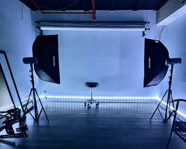 A photography studio with lighting equipment positioned around a central stool on a dark floor.