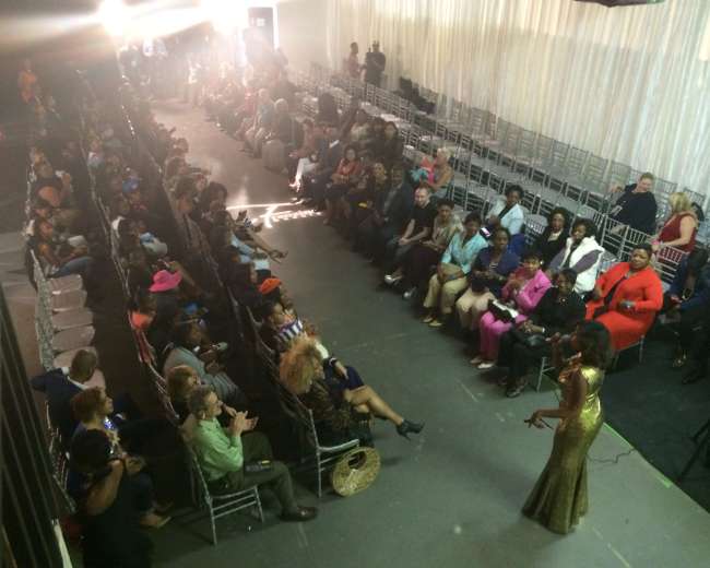 A crowd of seated audience members listens to a speaker at an event in a spacious venue.