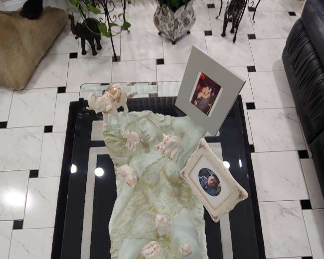 The image shows a decorative coffee table with a translucent sculpture of a reclining figure surrounded by several framed photos.