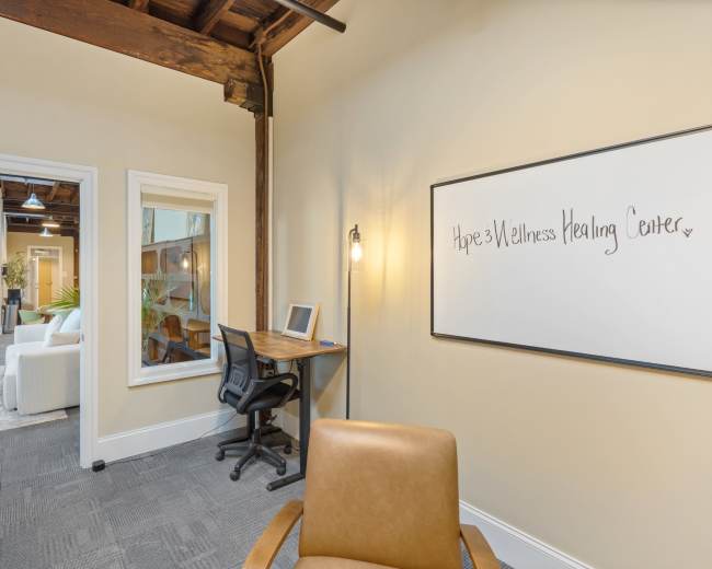 The image shows an office space with a desk and chair, a light fixture on the wall, and a whiteboard with "Hope's Wellness Healing Center" written on it.