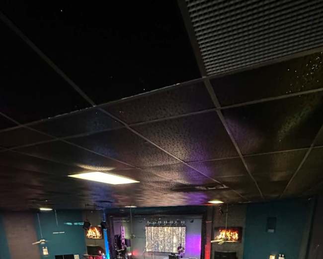 The image shows an empty event space with a stage at the front, surrounded by tables and chairs, and illuminated by multicolored lights.