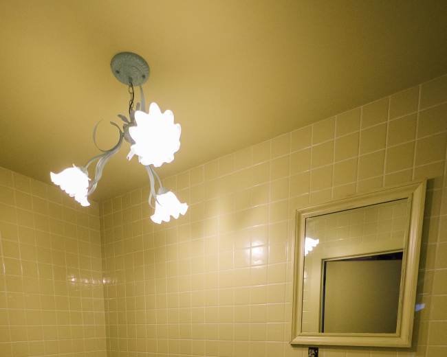 The image shows a small, tiled bathroom featuring a toilet, a sink, and a mirror, all in shades of green.