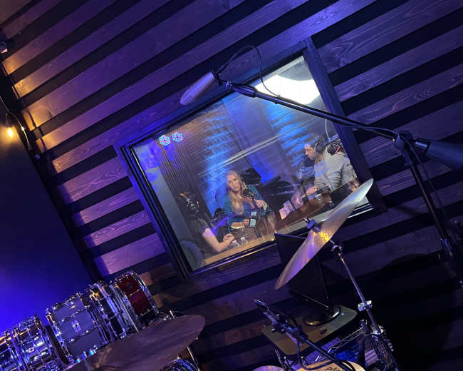 A view of two people sitting at a table inside a soundproof booth, with musical instruments in the foreground.