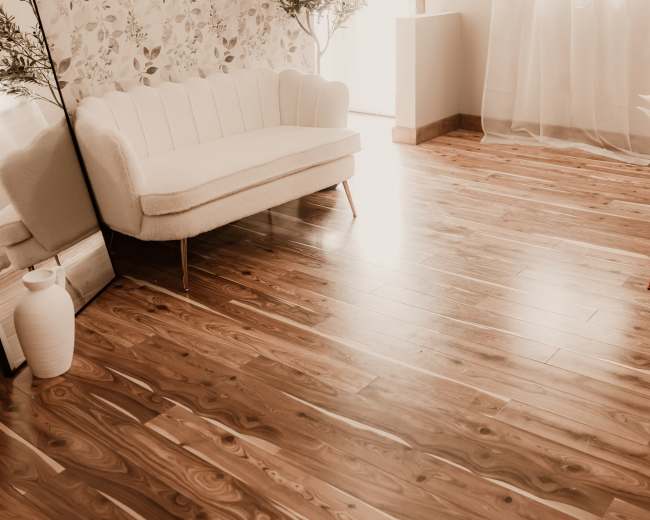 The image shows a bright, minimalist room with a floral wallpaper accent wall, a white sofa, a large mirror, a potted plant, and wooden flooring.