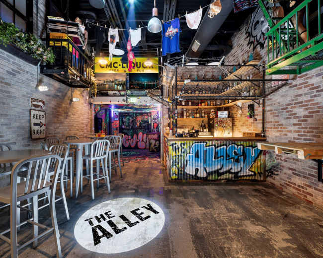 The interior of a lively urban-themed bar features exposed brick walls, colorful graffiti, and a bar area with high-top seating.