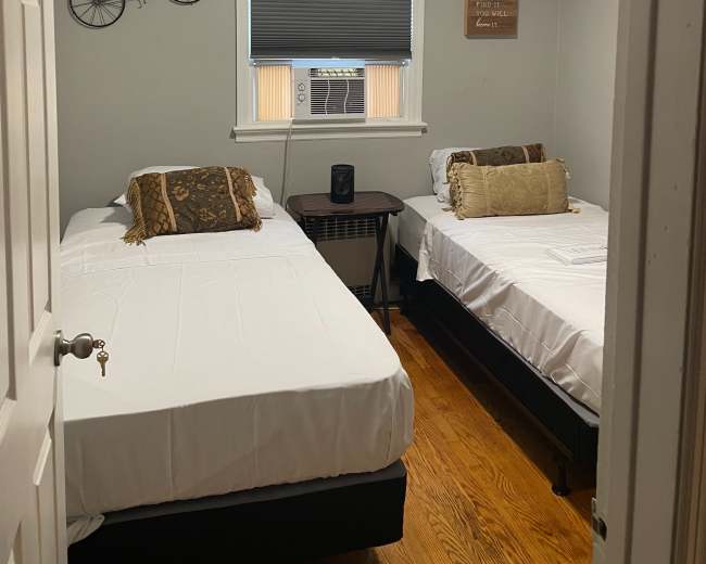 The image shows a small bedroom with two single beds, a side table, and decorative items on the walls.