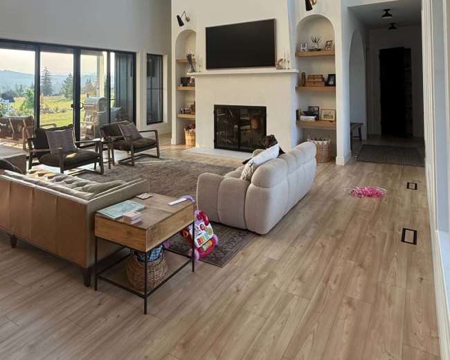The image shows a spacious living room with large windows, a high ceiling, a central fireplace, and a comfortable seating area.