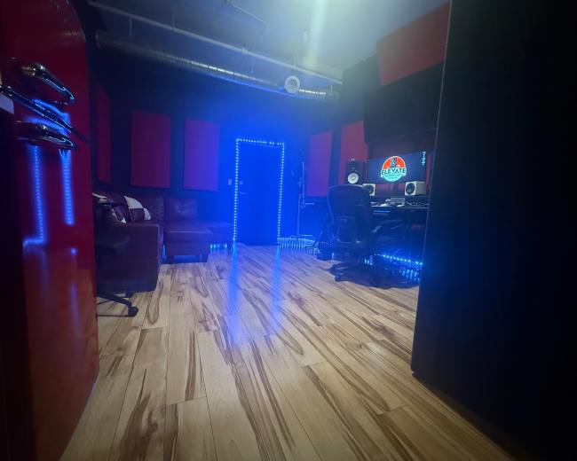 The image shows a music studio with a computer workstation, a dark couch, and blue LED lighting along the floor.