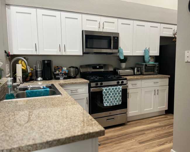 The image shows a modern kitchen with white cabinets, a granite countertop, stainless steel appliances, and a blue decorative towel hanging on the oven.