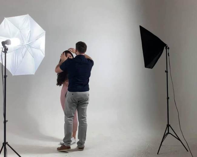 A man and a woman are posing closely together in a photography studio with softbox lights on either side.