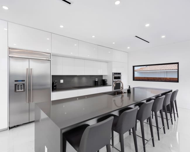 The kitchen features sleek white cabinetry, a large gray island with seating, and modern stainless steel appliances.