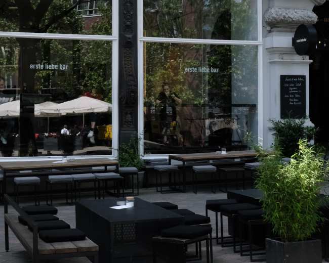 A modern outdoor seating area features black benches and tables in front of a building with large windows and greenery.