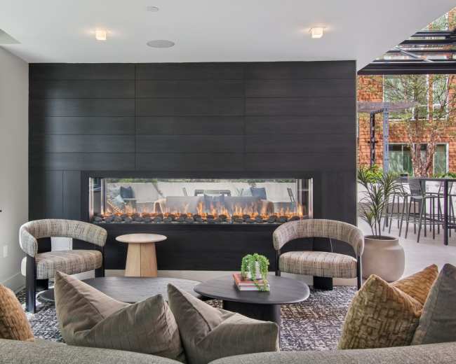 The image shows a modern living space featuring a sleek, linear fireplace against a black wall with two contemporary chairs and a low table arranged in front of it.