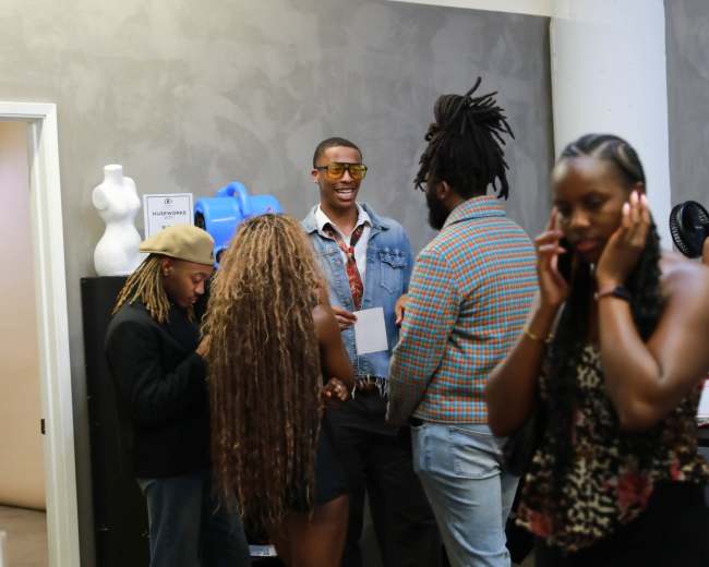 A group of people stands in a modern indoor space, engaged in conversation while one individual looks at their phone.