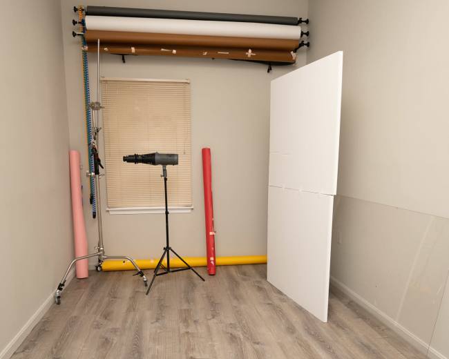 A photography studio with a backdrop setup, a light stand, and rolled paper in pink and yellow against a gray wall and floor.