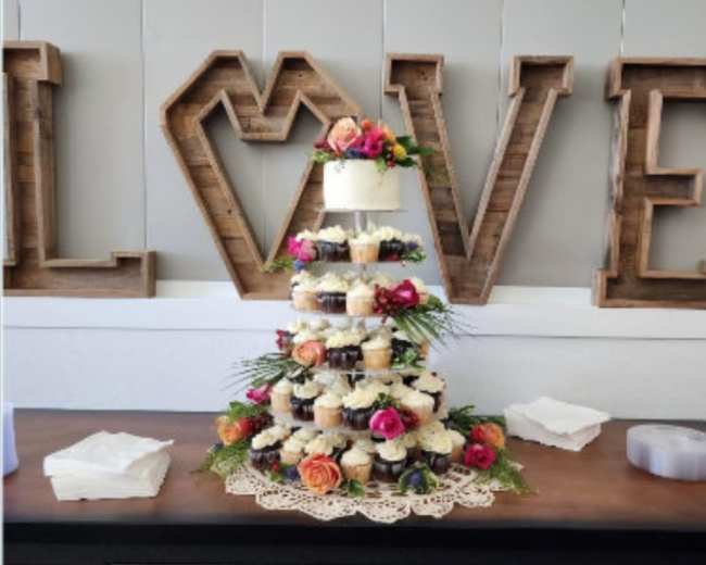 A tiered cupcake display decorated with flowers stands in front of large wooden letters spelling "LOVE."