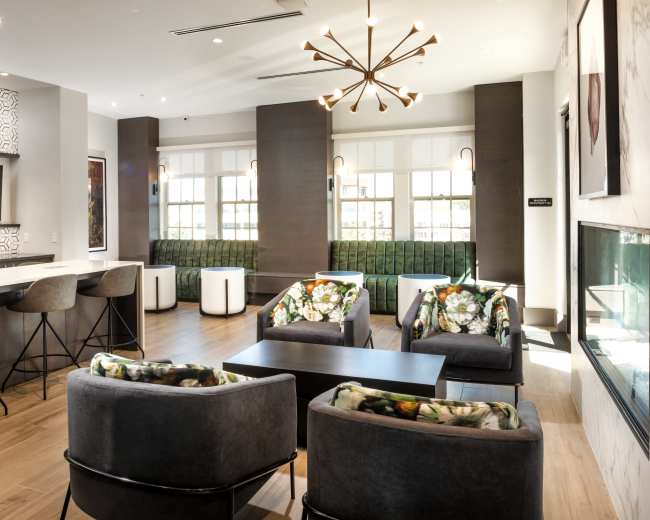 The image shows a modern lounge area with comfortable seating, a bar-like counter, and large windows letting in natural light.