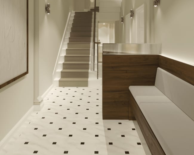 The image shows a spacious hallway featuring a staircase on the right, a wooden bench along the left wall, and decorative wall sconces illuminating the area.