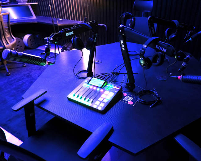 The image shows a recording studio with an octagonal table equipped with multiple microphones and headphones.