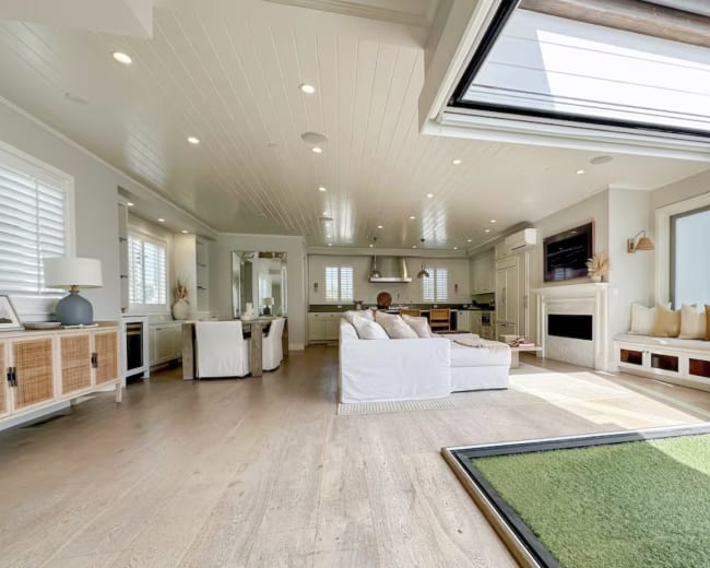 A spacious living area features a large white sectional sofa, a sleek kitchen, and sliding glass doors that open to a green outdoor space.