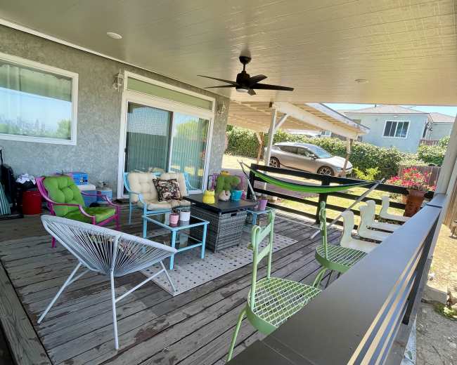 The image shows a covered outdoor patio with various colorful chairs, a coffee table, and a view of a car parked nearby.