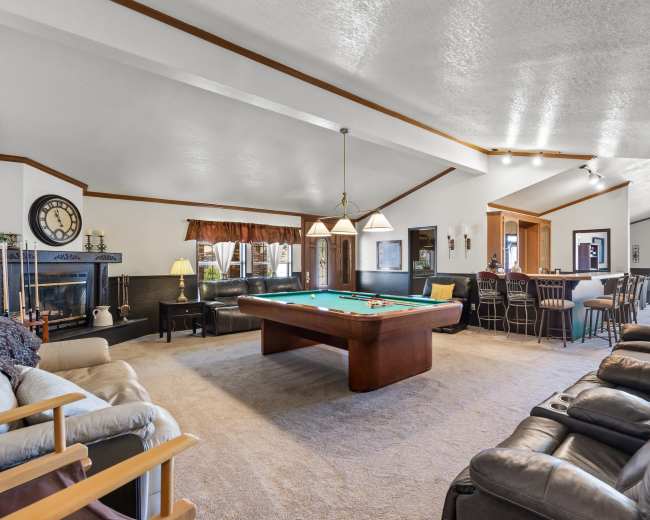 The spacious living area features a billiard table at the center, surrounded by seating options and a bar in the background.