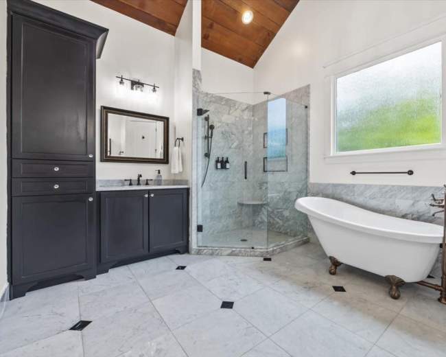The image shows a bathroom featuring a freestanding bathtub, a glass shower enclosure, and marble flooring.