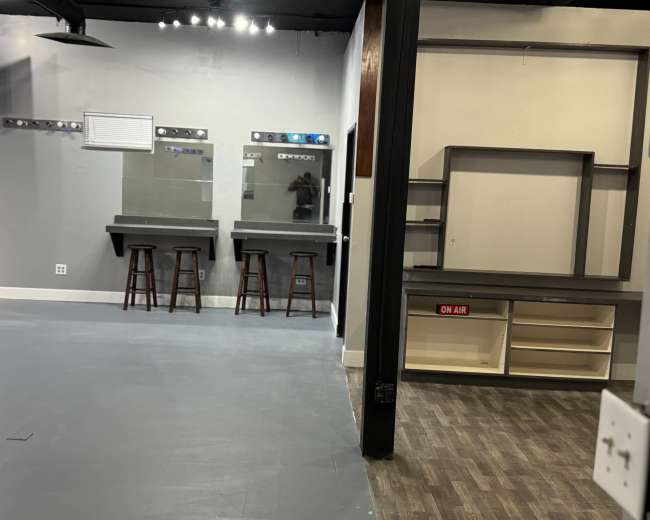 The image shows an empty room with two mirrors and stools against one wall, and a vacant shelf area with an "ON AIR" sign on another wall.