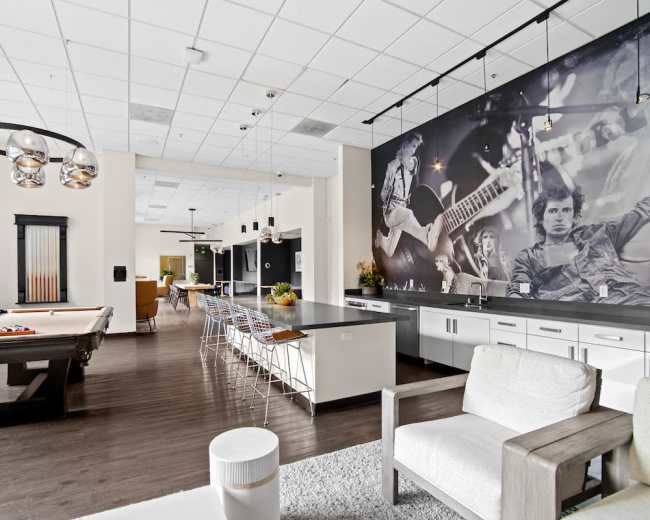 The image shows a modern recreational room with a pool table, a kitchen island with bar stools, and a large mural on the wall featuring musicians.