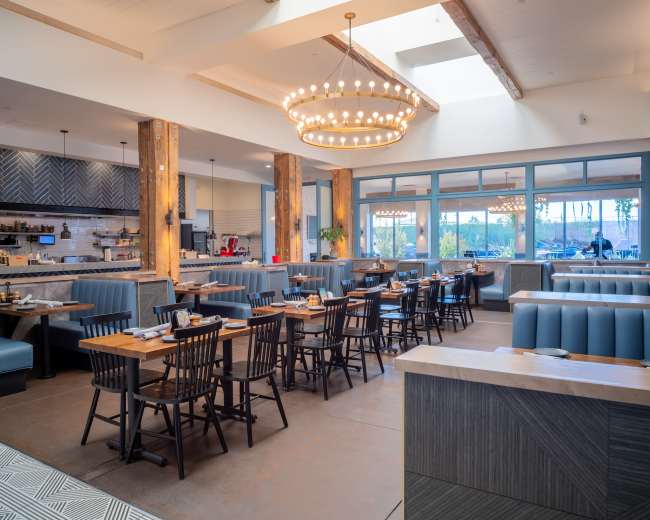 The image depicts a modern restaurant interior featuring blue booths, wooden tables, and a large chandelier.