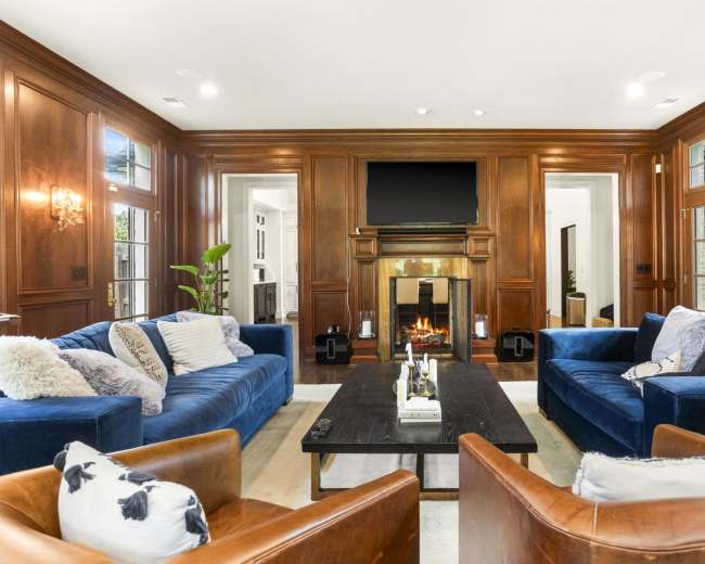 The living room features dark wooden paneling, a fireplace, and blue upholstered sofas arranged around a coffee table.