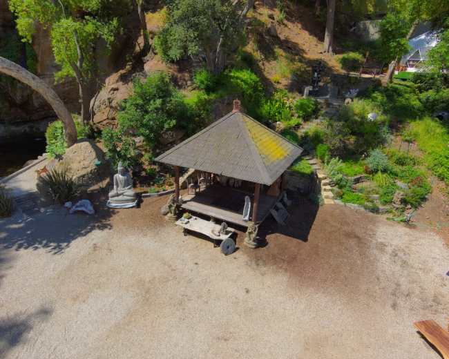 The image shows a gazebo surrounded by greenery and sculptures in a landscaped outdoor area.