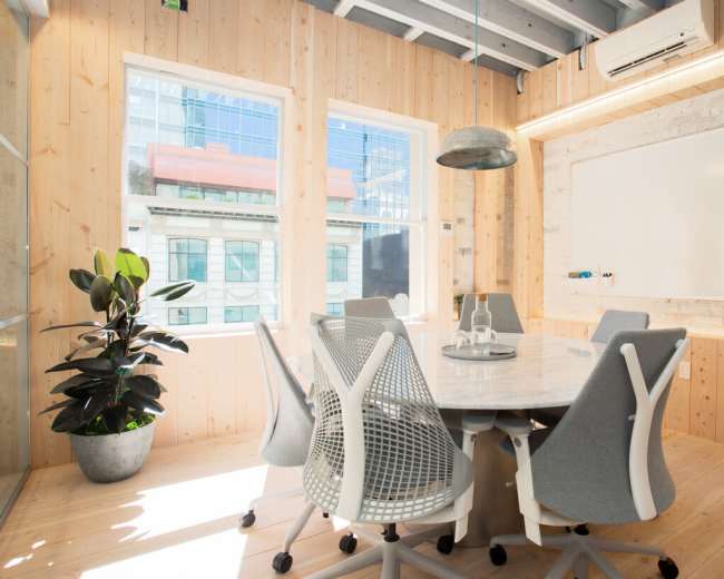 The image shows a modern conference room with a round marble table surrounded by ergonomic chairs, large windows, and wooden paneling.