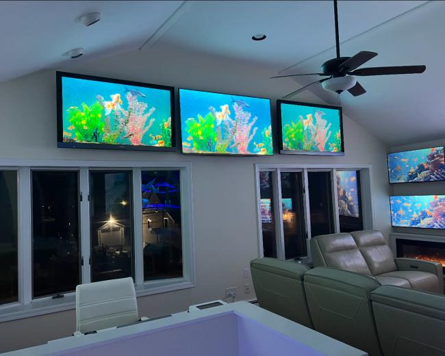 The room features multiple large screens displaying vibrant underwater scenes, with modern furniture and large windows visible.