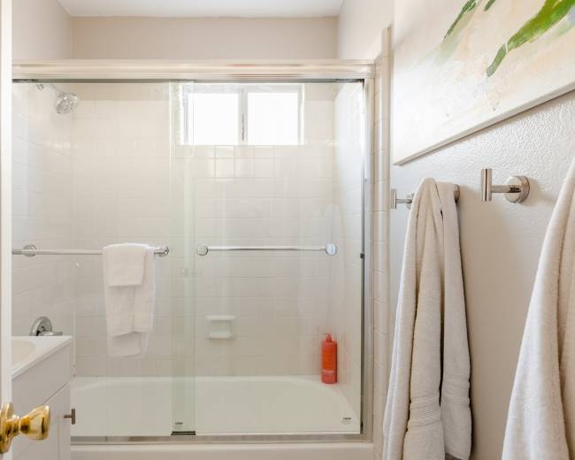 The image shows a clean bathroom with a glass shower enclosure, two white towels hanging on rods, and a small sink next to it.