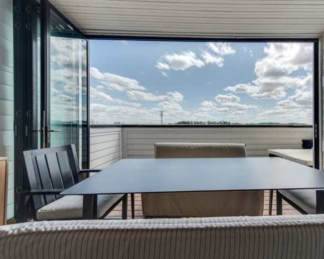 A modern outdoor patio features a table and chairs with large sliding doors opening to a view of a cloudy sky and landscape.