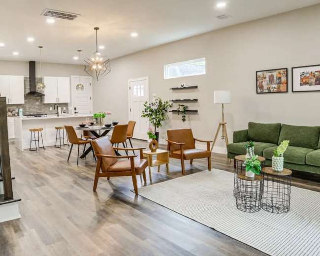 The image shows a modern living space featuring a combined living and dining area with a kitchen visible in the background, along with a staircase on the left side.