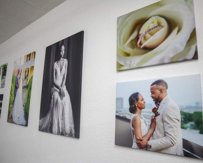 The image shows a wall displaying a collage of wedding photographs and a close-up of a ring on a rose.