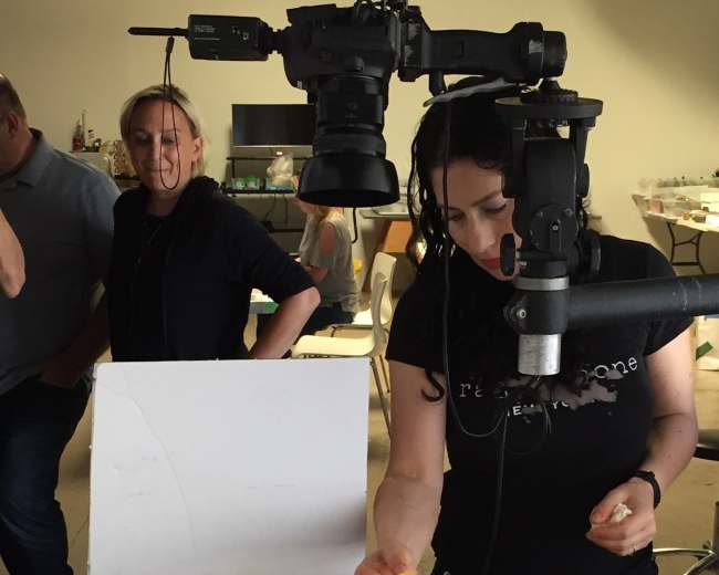 A woman garnishes a plate of salad with salmon under a camera set up in a photography studio.