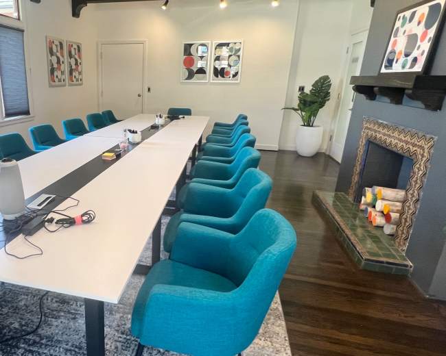 A large conference room features a long white table surrounded by teal chairs, a fireplace, and artwork on the walls.
