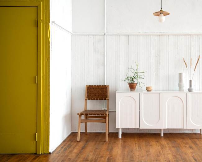 A simple room features a white cabinet and a wooden chair next to a green door against a light-colored wall.