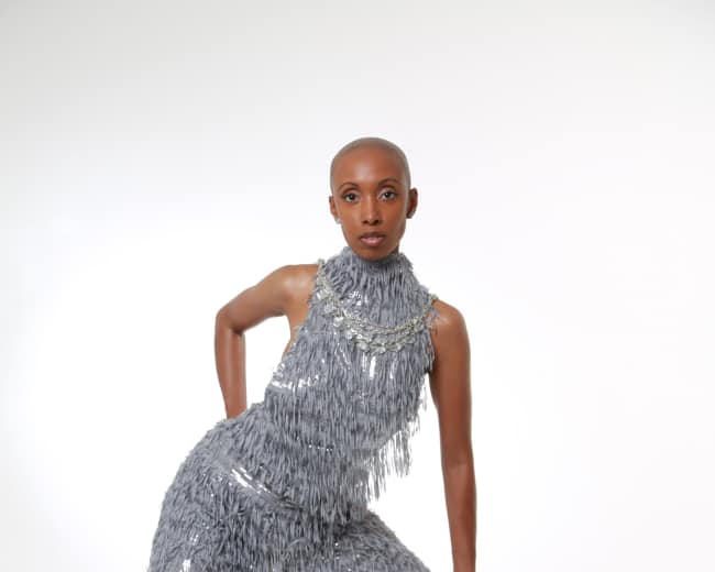A model poses in a textured gray outfit with fringes against a plain white background.