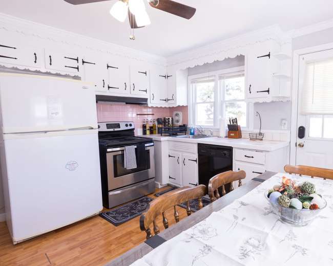 The image shows a kitchen with white cabinets, a black and stainless steel stove, a refrigerator, and a dining table set with a centerpiece.