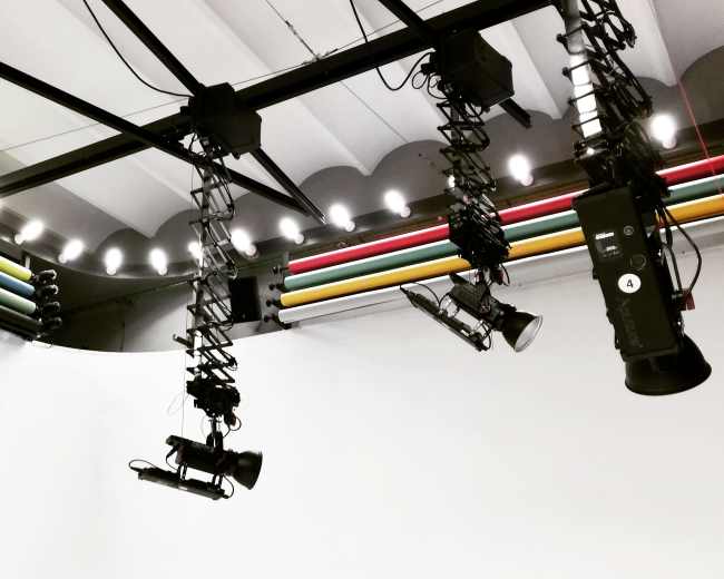 A studio ceiling with suspended lighting rigs and colorful cables.