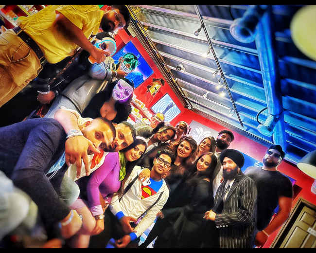 A group of people dressed in various costumes poses together in a vibrant indoor space.