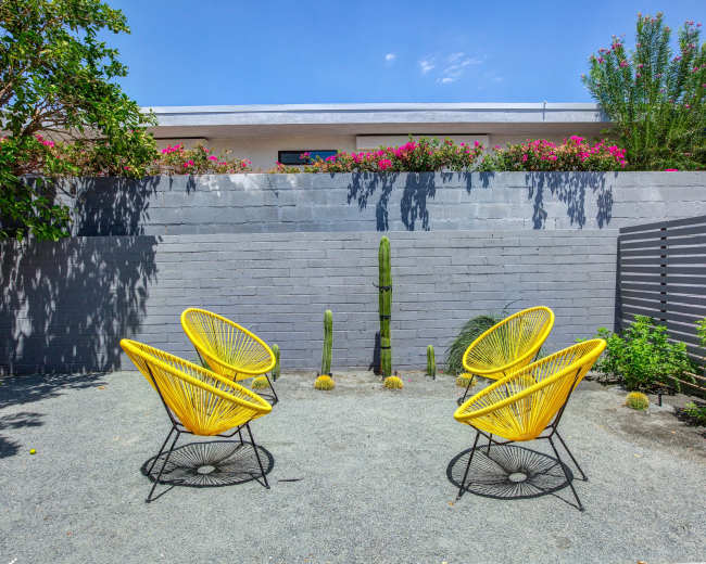 A landscaped outdoor space features four yellow chairs arranged around small cactus plants on gravel.