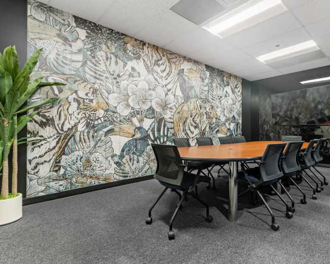 A modern conference room features a large wooden table surrounded by black chairs, with a decorative wall mural of tigers and flowers.