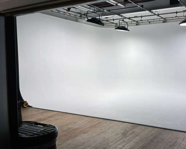 The image shows a spacious photography studio with a seamless white backdrop and overhead lighting.